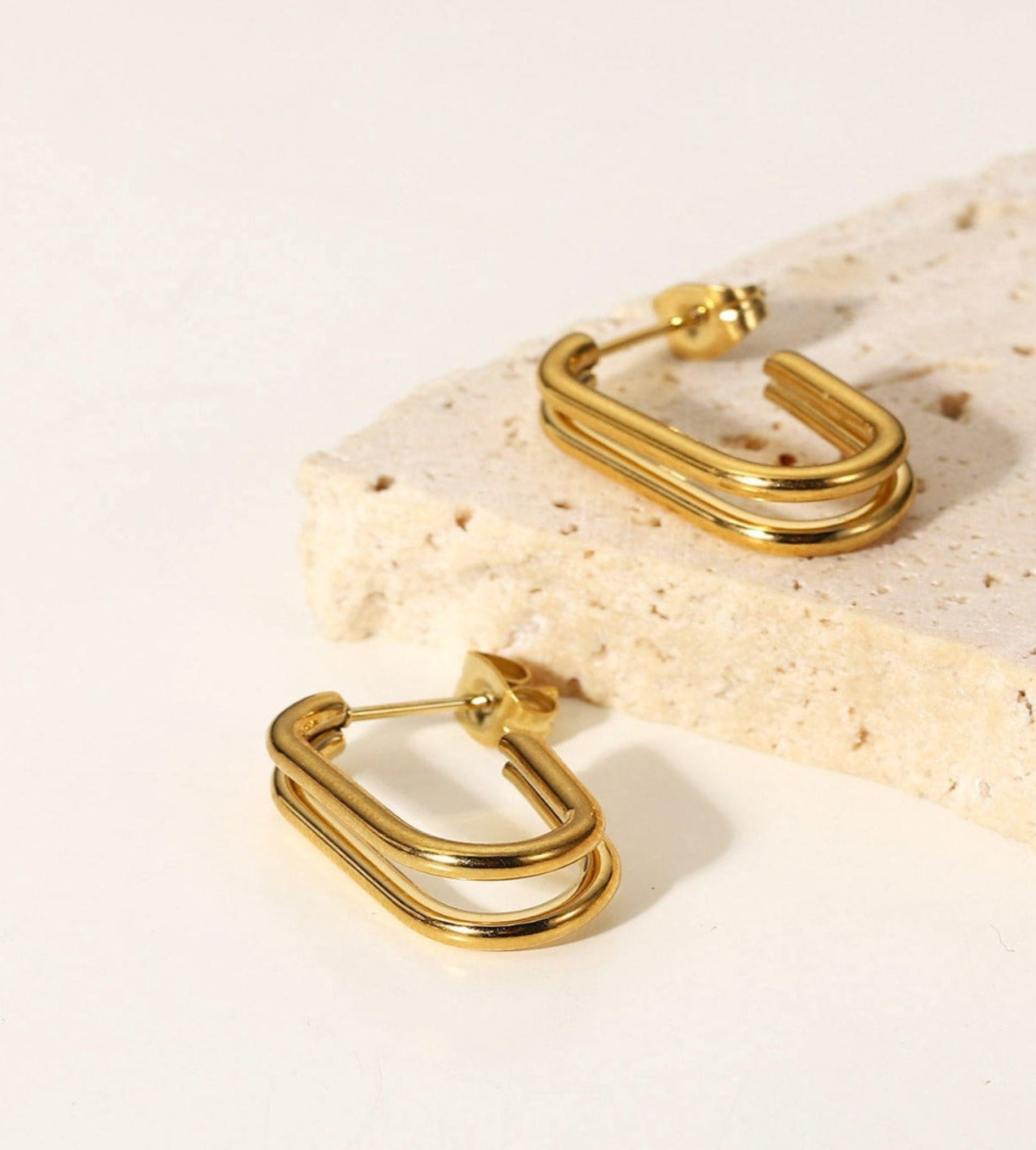 Core CC gold triple-bar hoop earrings on a stone and white backdrop